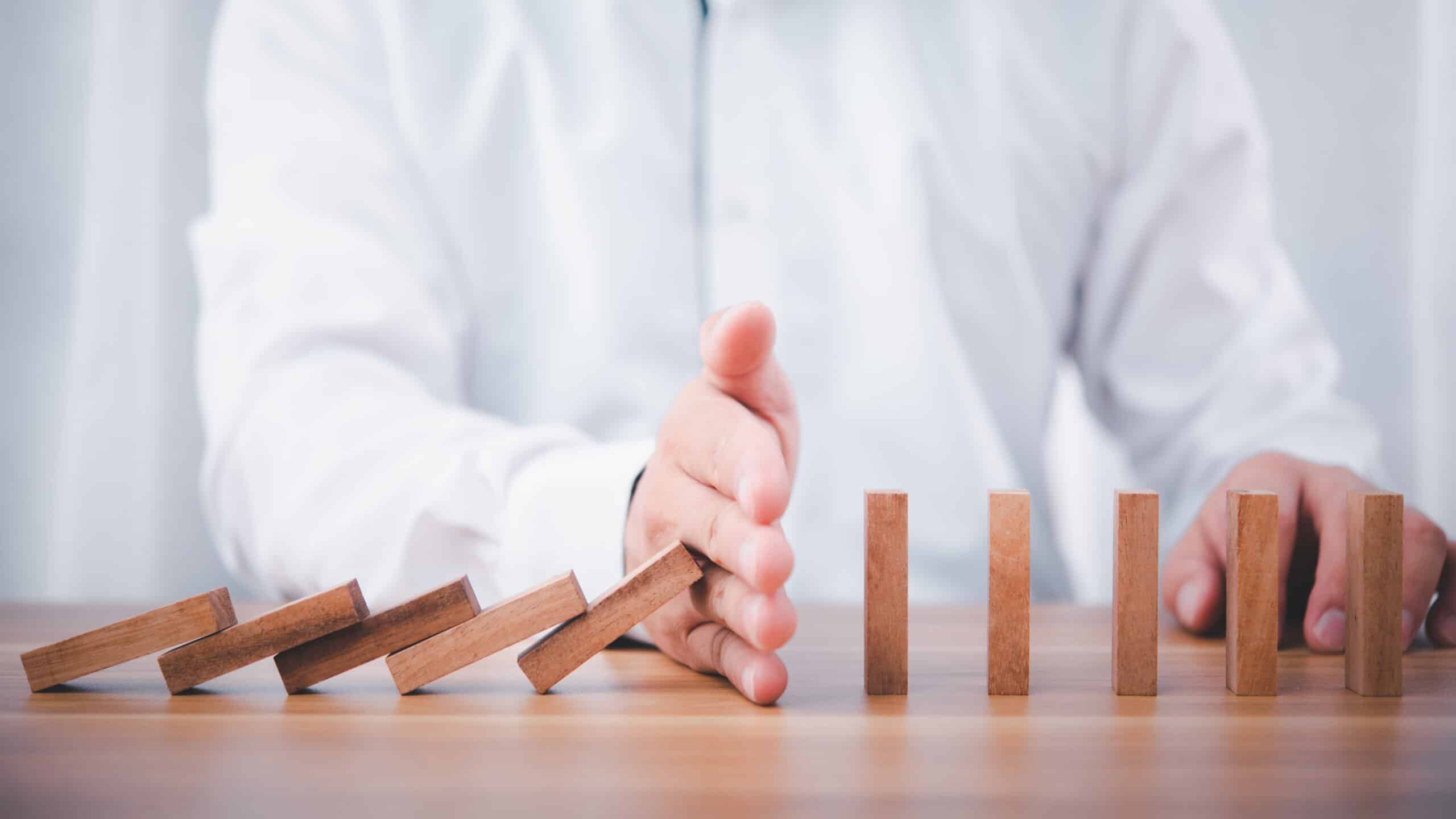 Businessman hand stop falling down of wood block .planing and strategy business disruption concept.